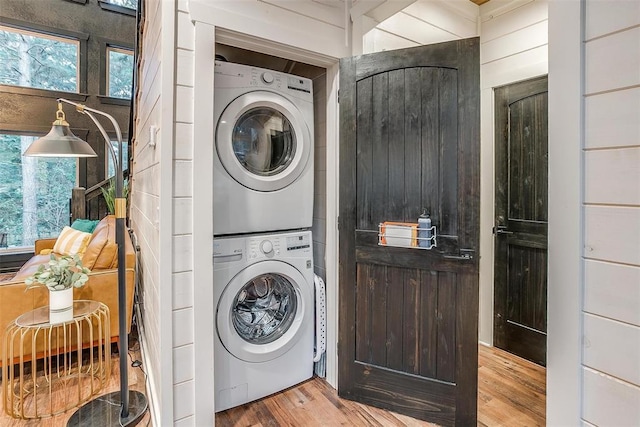 laundry room featuring hardwood / wood-style floors, wooden walls, and stacked washer and clothes dryer