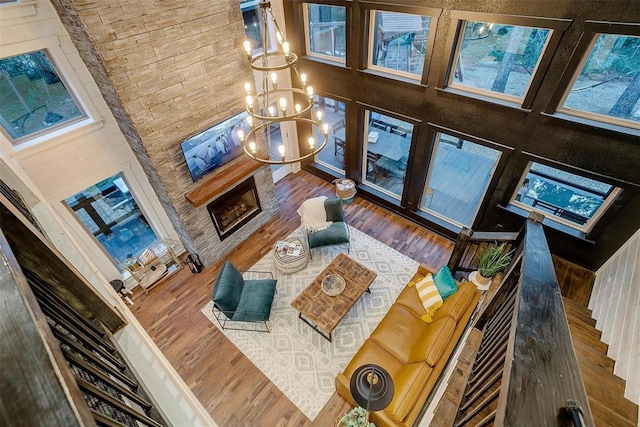 living room featuring a stone fireplace, dark hardwood / wood-style floors, a high ceiling, and an inviting chandelier