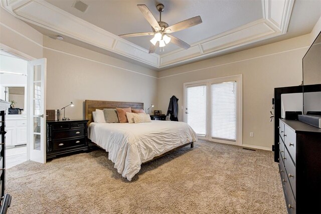 bedroom with connected bathroom, ceiling fan, a tray ceiling, light carpet, and ornamental molding