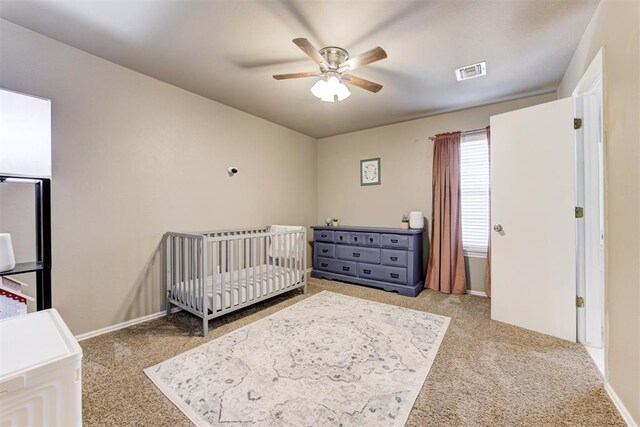 bedroom featuring ceiling fan, light colored carpet, and a crib