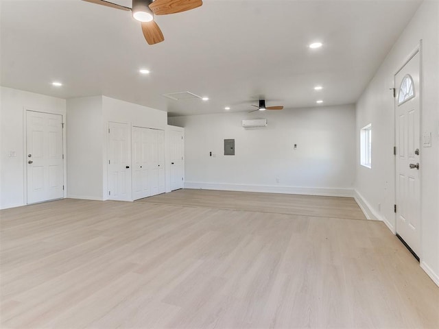 unfurnished room featuring a wall mounted air conditioner, ceiling fan, electric panel, and light hardwood / wood-style flooring