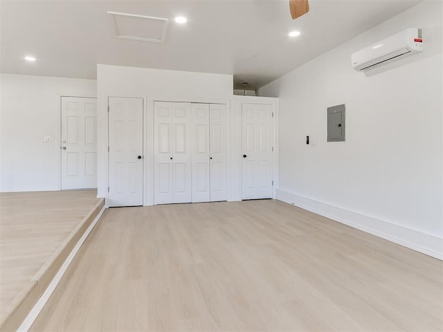 unfurnished bedroom featuring a wall unit AC, electric panel, ceiling fan, and light wood-type flooring