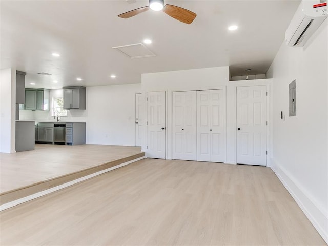 unfurnished living room featuring a wall unit AC, electric panel, ceiling fan, and light hardwood / wood-style floors