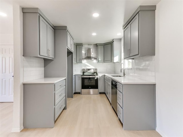 kitchen with sink, light hardwood / wood-style flooring, wall chimney exhaust hood, gray cabinets, and stainless steel appliances