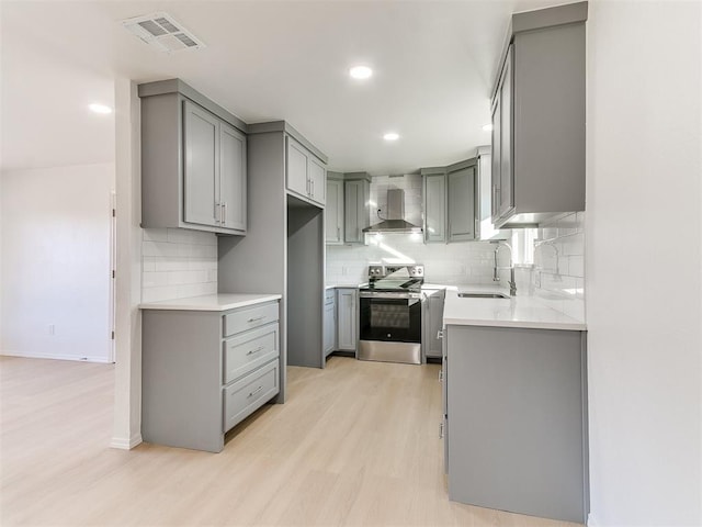 kitchen with gray cabinetry, stainless steel electric stove, sink, wall chimney range hood, and light hardwood / wood-style flooring