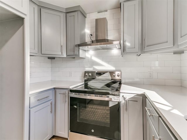 kitchen with stainless steel range with electric stovetop, wall chimney exhaust hood, gray cabinets, and tasteful backsplash