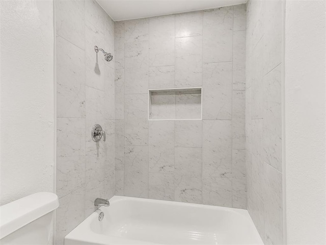 bathroom featuring tiled shower / bath combo and toilet