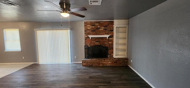 unfurnished living room featuring ceiling fan, built in features, dark wood-type flooring, and a brick fireplace