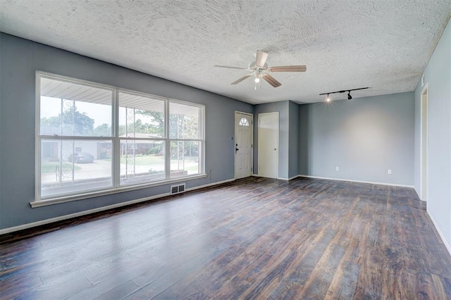 empty room featuring a textured ceiling, dark hardwood / wood-style floors, track lighting, and ceiling fan