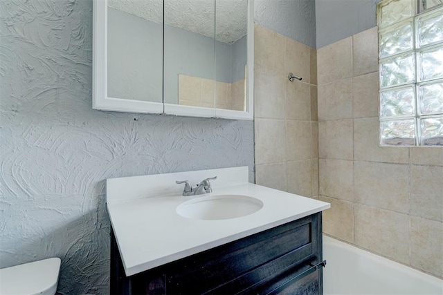 full bathroom featuring tiled shower / bath, vanity, and toilet