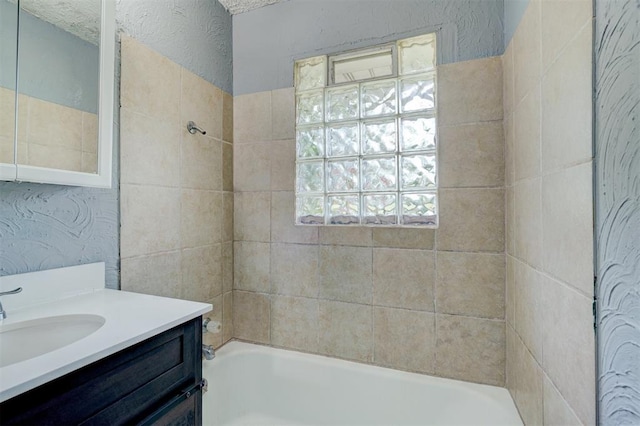 bathroom with a textured ceiling, vanity, and tiled shower / bath combo