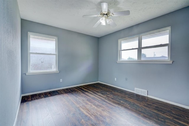 spare room featuring dark hardwood / wood-style floors, a textured ceiling, and a wealth of natural light