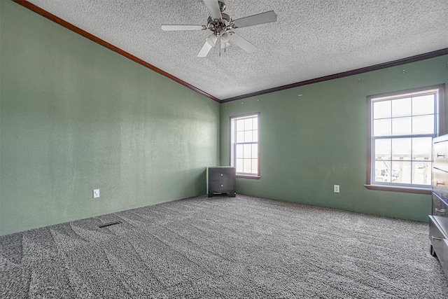 empty room with lofted ceiling, ceiling fan, carpet floors, ornamental molding, and a textured ceiling