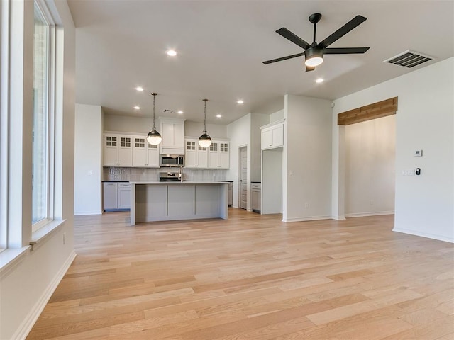 kitchen featuring white cabinetry, light hardwood / wood-style flooring, a spacious island, decorative light fixtures, and appliances with stainless steel finishes