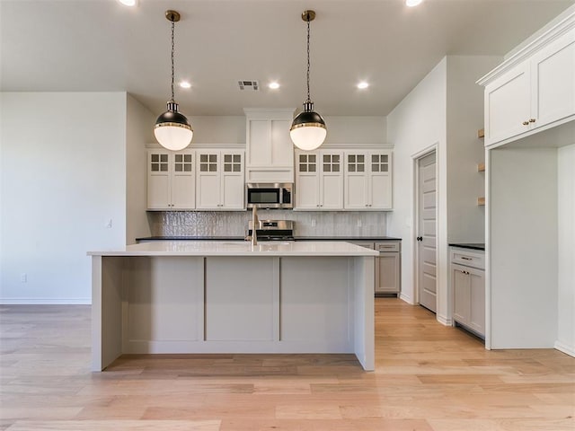 kitchen with white cabinetry, stainless steel appliances, backsplash, pendant lighting, and light hardwood / wood-style floors