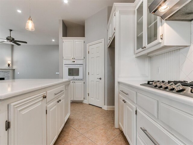 kitchen featuring stainless steel gas cooktop, ceiling fan, oven, white cabinetry, and range hood