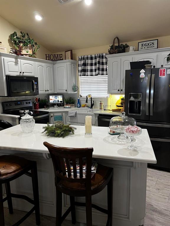 kitchen featuring a breakfast bar, white cabinets, refrigerator with ice dispenser, and stainless steel electric range