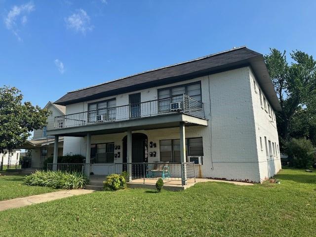 view of front of property with covered porch, a balcony, and a front lawn