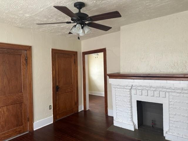 unfurnished living room featuring a stone fireplace, ceiling fan, dark wood-type flooring, and a textured ceiling