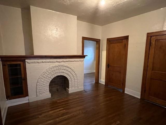 unfurnished living room with dark wood-type flooring and a brick fireplace