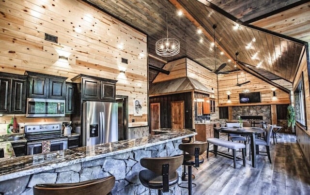 kitchen featuring dark wood-type flooring, high vaulted ceiling, dark stone countertops, wood walls, and appliances with stainless steel finishes