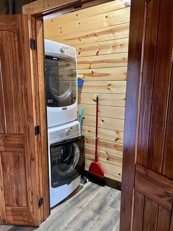 laundry room featuring wood walls, light wood-type flooring, and stacked washer / dryer