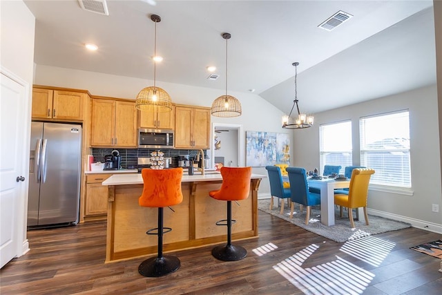 kitchen with stainless steel appliances, dark hardwood / wood-style floors, an island with sink, pendant lighting, and vaulted ceiling