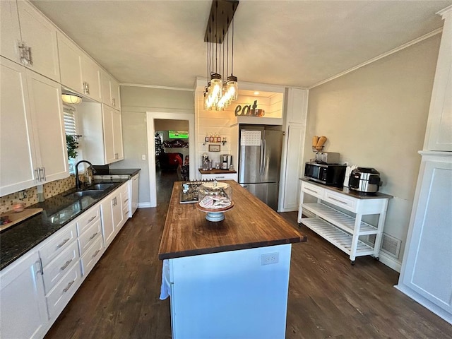 kitchen with stainless steel refrigerator, white cabinetry, wood counters, decorative light fixtures, and a kitchen island