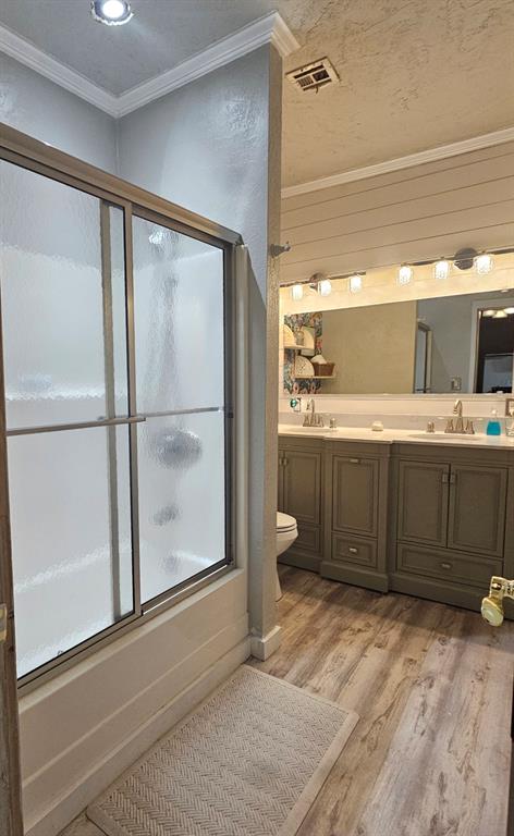 full bathroom featuring combined bath / shower with glass door, ornamental molding, vanity, hardwood / wood-style flooring, and toilet