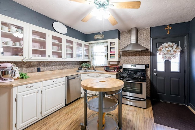 kitchen featuring wall chimney exhaust hood, a healthy amount of sunlight, white cabinetry, and appliances with stainless steel finishes