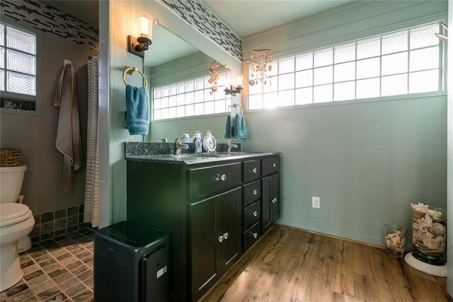 full bath with toilet, a sink, double vanity, and wood finished floors