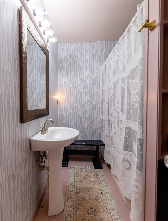 full bath with curtained shower, a sink, and wallpapered walls