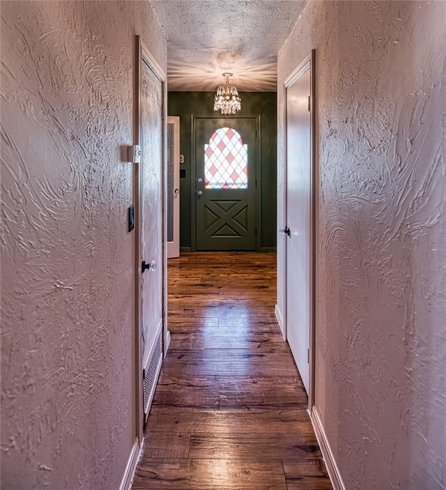 entryway with a textured ceiling, a textured wall, hardwood / wood-style flooring, and a notable chandelier