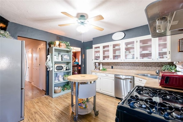 kitchen featuring a ceiling fan, appliances with stainless steel finishes, light wood-type flooring, white cabinetry, and a sink