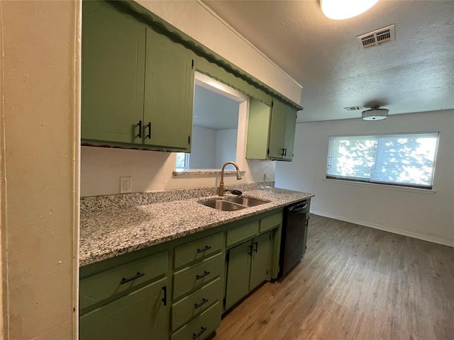 kitchen featuring visible vents, black dishwasher, light wood-type flooring, green cabinetry, and a sink