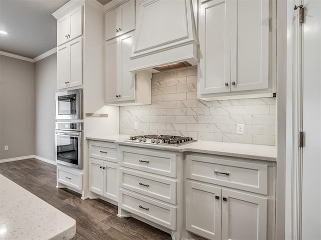 kitchen with appliances with stainless steel finishes, dark hardwood / wood-style flooring, light stone counters, ornamental molding, and white cabinets