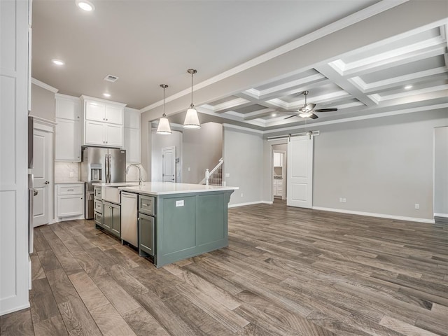 kitchen with hanging light fixtures, a barn door, a center island with sink, white cabinets, and hardwood / wood-style flooring