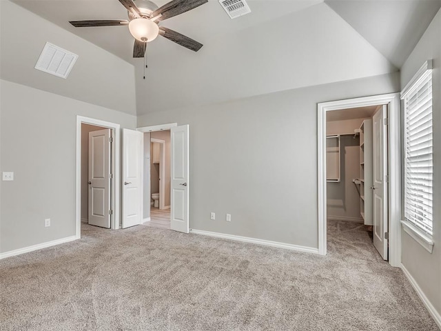 unfurnished bedroom with lofted ceiling, light carpet, ceiling fan, a spacious closet, and connected bathroom