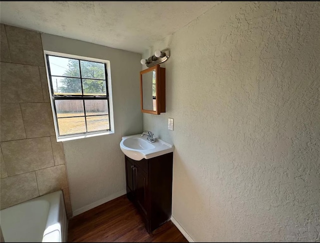 bathroom featuring wood-type flooring, vanity, a tub to relax in, and a textured ceiling