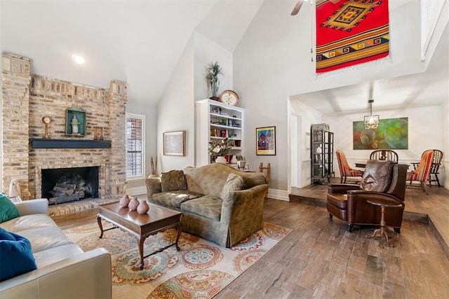 living room with hardwood / wood-style floors, ceiling fan, a fireplace, and high vaulted ceiling