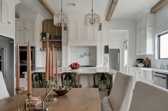 kitchen with beamed ceiling, pendant lighting, white cabinetry, and stainless steel appliances