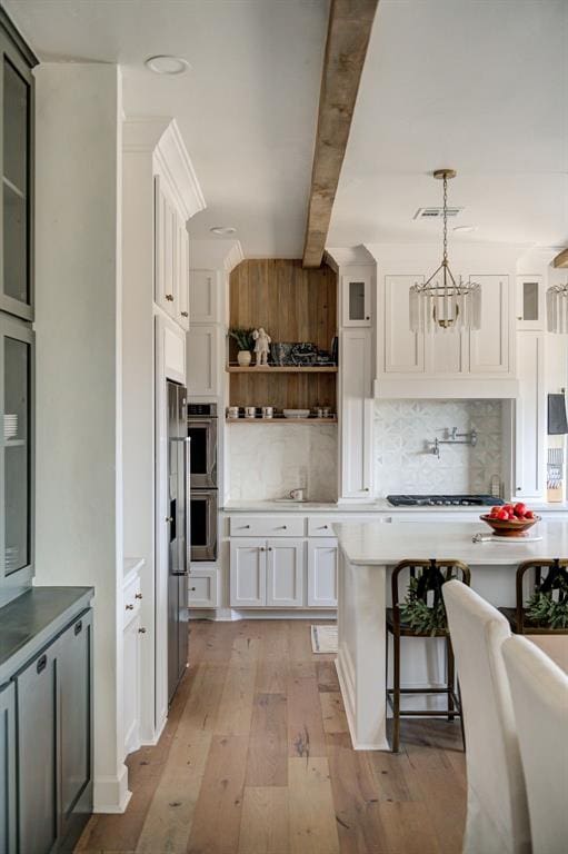 kitchen featuring appliances with stainless steel finishes, decorative light fixtures, white cabinetry, light wood-type flooring, and beam ceiling