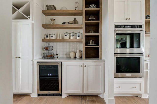 bar featuring white cabinets, beverage cooler, double oven, tasteful backsplash, and light hardwood / wood-style floors