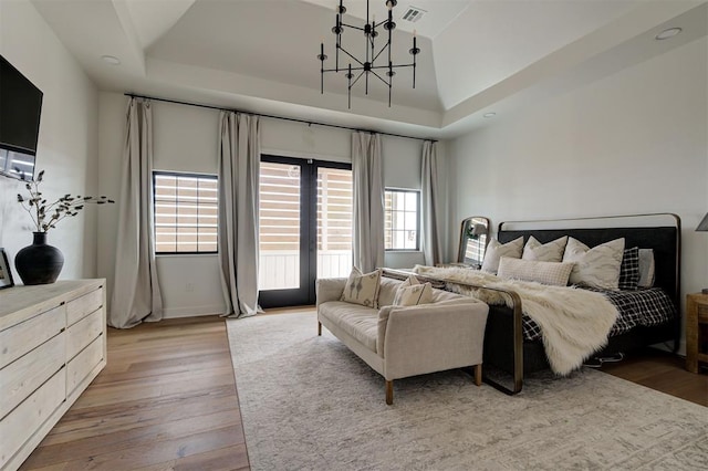 bedroom featuring light wood-type flooring, a tray ceiling, and multiple windows