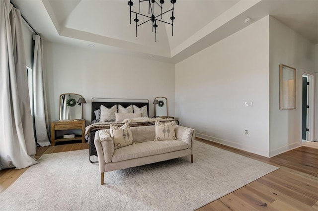 bedroom with a towering ceiling, wood-type flooring, a tray ceiling, and a chandelier