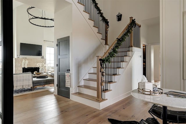 stairs with a high ceiling, wood-type flooring, and a stone fireplace