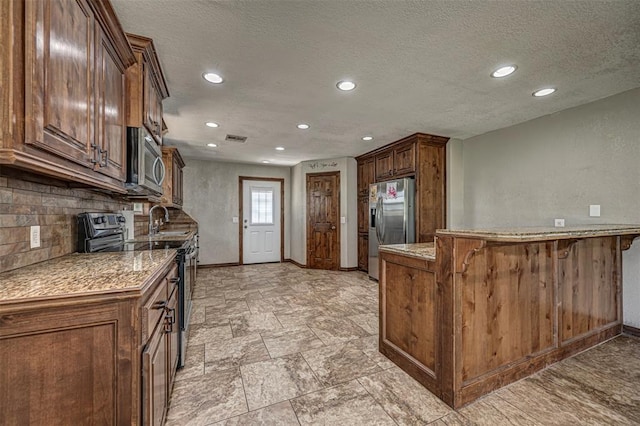 kitchen featuring backsplash, a breakfast bar area, a textured ceiling, kitchen peninsula, and stainless steel appliances