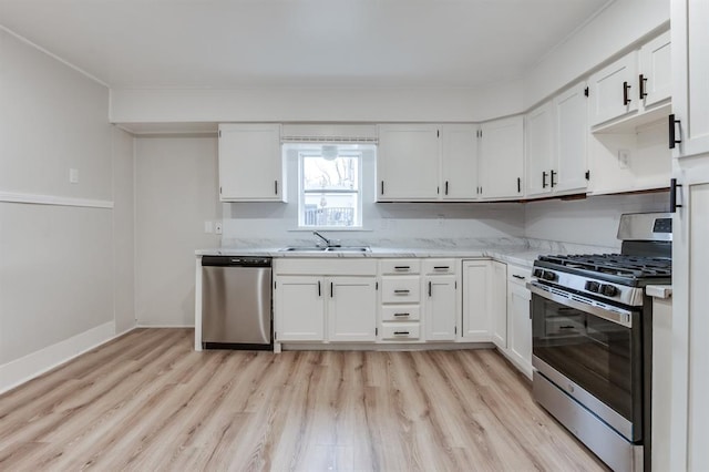 kitchen with appliances with stainless steel finishes, sink, white cabinets, light wood-type flooring, and light stone countertops