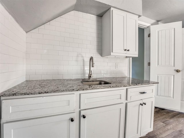 kitchen featuring light stone counters, sink, dark wood-type flooring, and vaulted ceiling