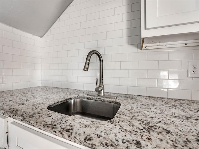 room details featuring backsplash, light stone countertops, sink, and white cabinets